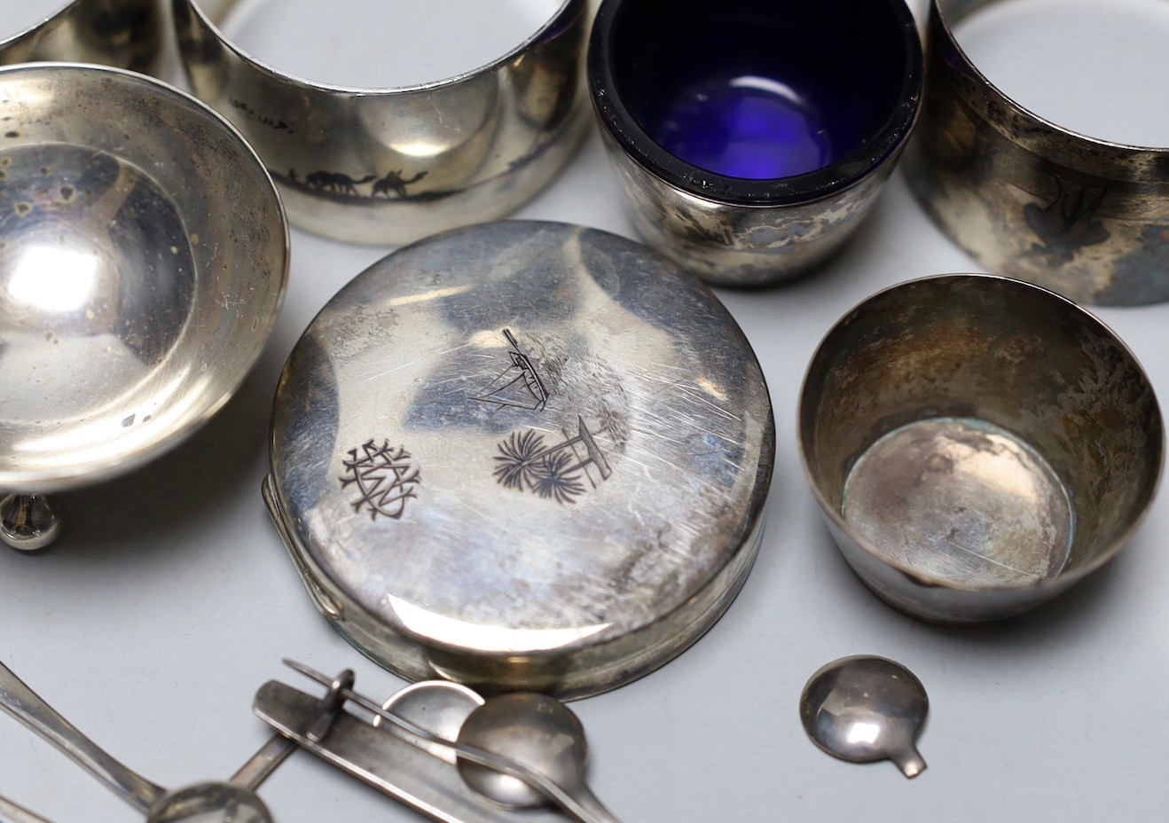 Thirteen assorted Iraq white metal and niello condiments, circular box, five similar napkin rings, a brooch and a pair of similar (damaged) candlesticks.